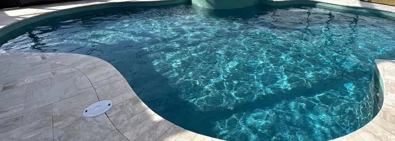 Pool surrounded by new marble decking inside a screen enclosure
